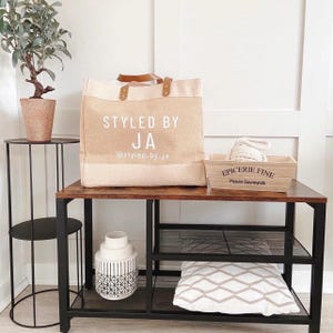 Puede incluir: Una bolsa de mano marr&oacute;n y beige con el texto "Styled by JA @styled_by_ja" en la parte delantera. La bolsa est&aacute; sobre una mesa de madera con una estanter&iacute;a de metal negro debajo. Hay un jarr&oacute;n de cer&aacute;mica blanco con un patr&oacute;n geom&eacute;trico en la estanter&iacute;a.