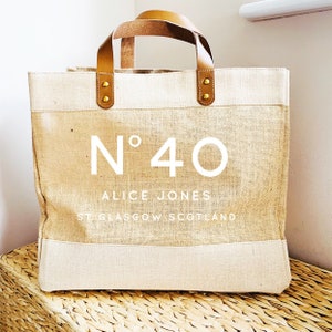 May include: A beige tote bag with brown leather handles and gold accents. The bag has a white logo that says "N&deg;40 ALICE JONES ST GLASGOW SCOTLAND".