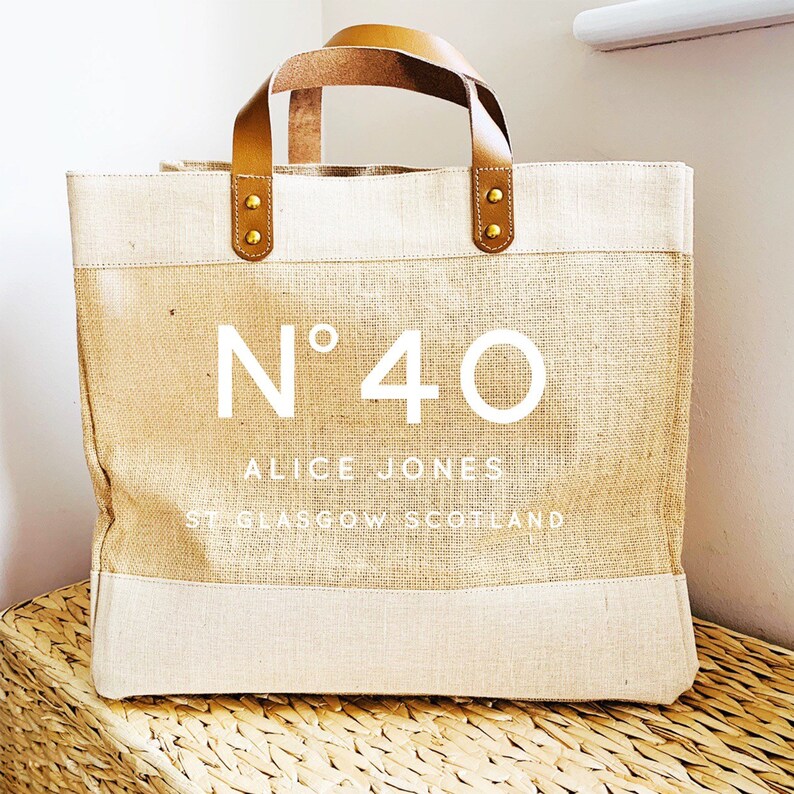 May include: A beige tote bag with brown leather handles and gold accents. The bag has a white logo that says "N&deg;40 ALICE JONES ST GLASGOW SCOTLAND".