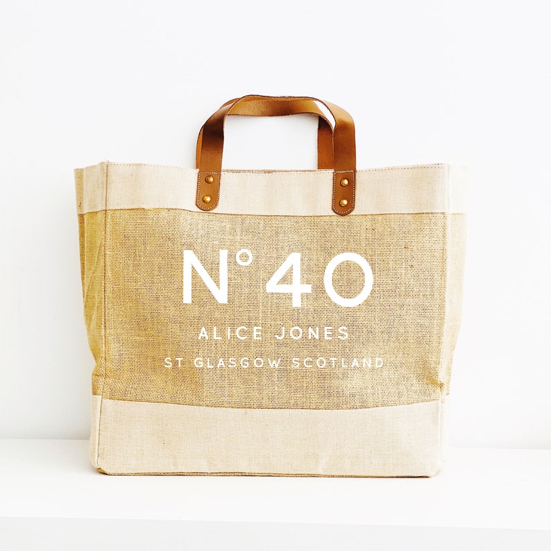 May include: A beige tote bag with brown leather handles and gold accents. The bag has a white logo that says "N&deg;40 ALICE JONES ST GLASGOW SCOTLAND".