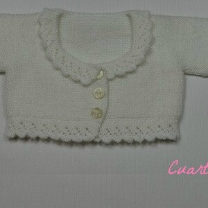 May include: A white knitted cardigan with a scalloped collar and cuffs. The cardigan has a button closure and is made of a soft, lightweight yarn.