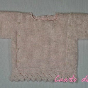 Pode incluir: Um suéter de tricô rosa para bebê com uma bainha festonada e botões perolados.
