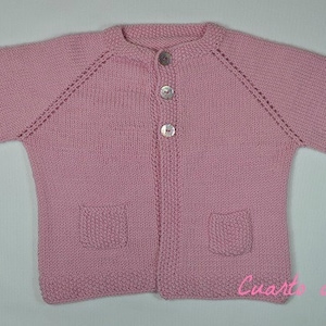 May include: A pink knitted cardigan with a button closure, two pockets, and a slightly flared hem.
