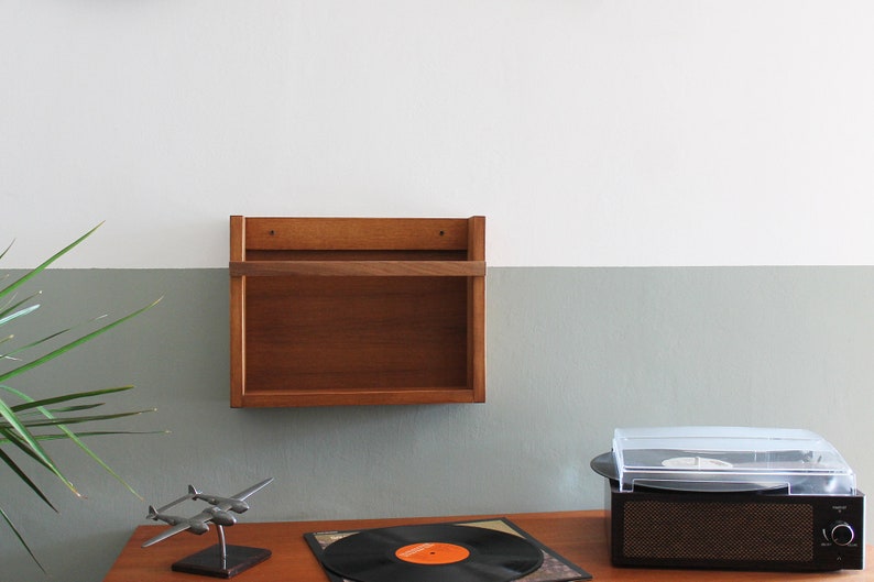 May include: A wooden wall shelf with two shelves, a record player with a clear lid, a model airplane, and a vinyl record on a wooden table.