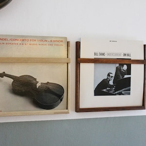 May include: Two vinyl record albums displayed on a wall mounted record rack. The album on the left features a black and white image of a violin. The album on the right features a black and white image of a man playing a piano. The album on the left has the text "HANDEL/CONCERTO FOR VIOLIN - B MINOR" and "VIOLIN SONATAS 3 & 6/ MUSIC MINUS ONE VIOLIN". The album on the right has the text "BILL EVANS - UNDERCURRENT - JIM HALL".