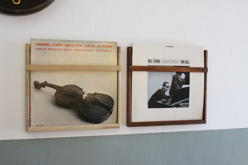 May include: Two vinyl record albums displayed on a wall mounted record rack. The album on the left features a black and white image of a violin. The album on the right features a black and white image of a man playing a piano. The album on the left has the text "HANDEL/CONCERTO FOR VIOLIN - B MINOR" and "VIOLIN SONATAS 3 & 6/ MUSIC MINUS ONE VIOLIN". The album on the right has the text "BILL EVANS - UNDERCURRENT - JIM HALL".