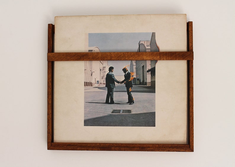 May include: A framed record album with a picture of two men shaking hands. The man on the right is on fire. The album cover is titled "The Dark Side of the Moon" by Pink Floyd.