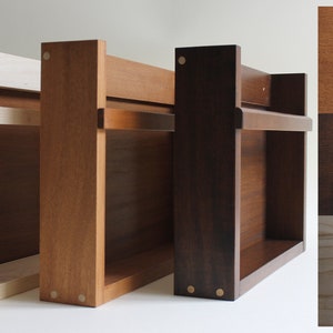 May include: Three wooden shelves in natural, teak, and walnut finishes. The shelves have a simple design with two shelves and a small lip on the top shelf. The shelves are made of solid wood and have a natural finish. The shelves are shown against a white background.