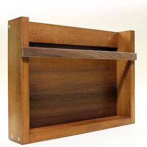 May include: A wooden wall-mounted shelf with a single shelf and a metal bar for hanging towels or other items. The shelf is made of a dark wood with a natural finish.