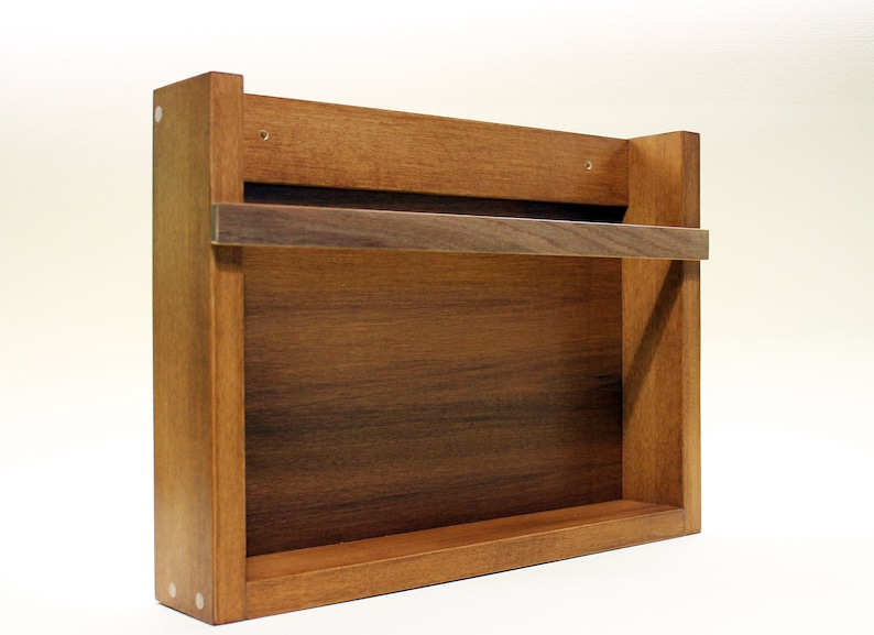 May include: A wooden wall-mounted shelf with a single shelf and a metal bar for hanging towels or other items. The shelf is made of a dark wood with a natural finish.
