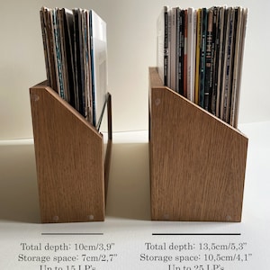 May include: Two wooden record storage shelves with angled sides. The shelf on the left holds 15 records and is 10 cm deep. The shelf on the right holds 25 records and is 13.5 cm deep.