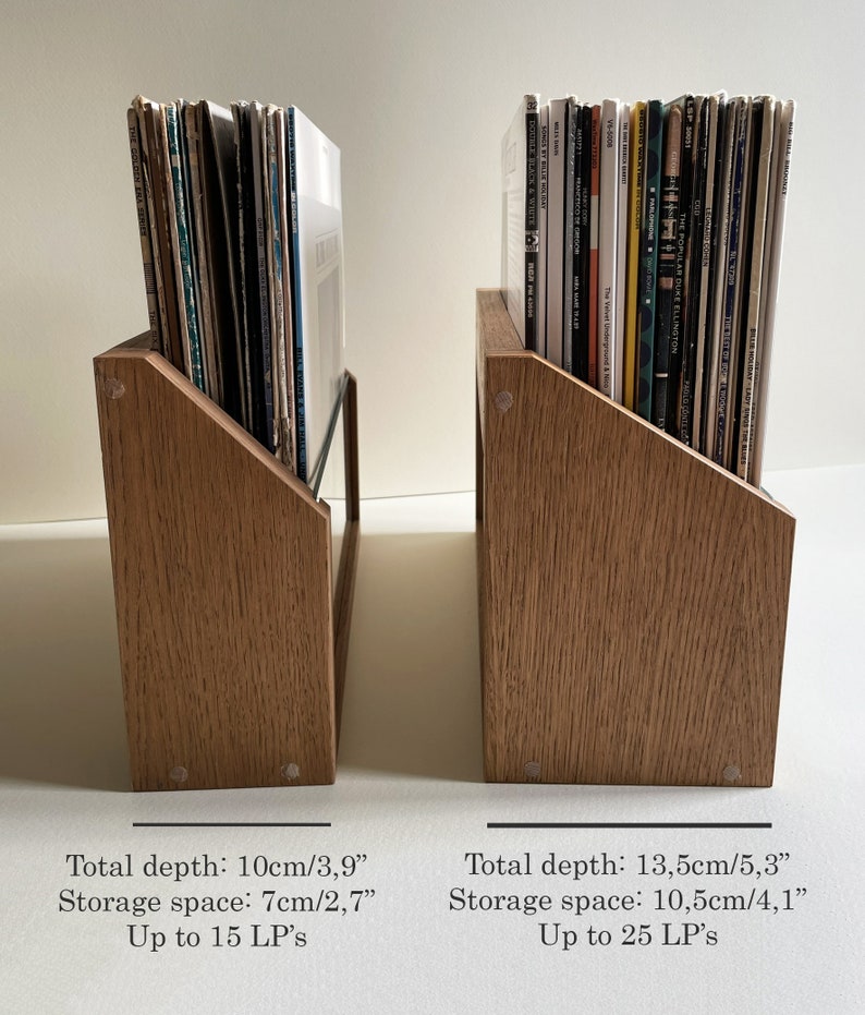 May include: Two wooden record storage shelves with angled sides. The shelf on the left holds 15 records and is 10 cm deep. The shelf on the right holds 25 records and is 13.5 cm deep.