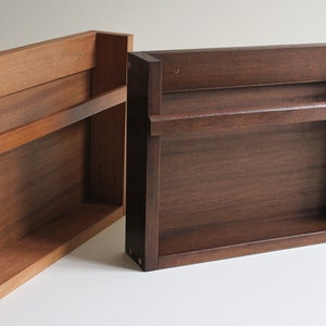 May include: Two wooden wall shelves, one with a single shelf and the other with two shelves. Both shelves are made of dark wood and have a simple, minimalist design.