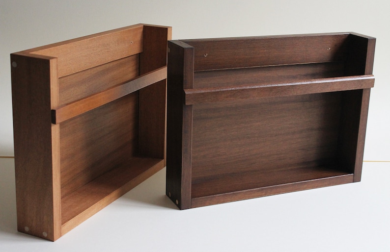 May include: Two wooden wall shelves, one with a single shelf and the other with two shelves. Both shelves are made of dark wood and have a simple, minimalist design.