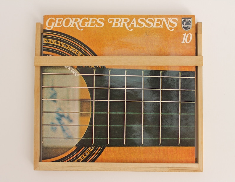 May include: A wooden record holder with a vinyl record inside. The record is by Georges Brassens and is a Philips recording. The record cover is orange and brown with a guitar on the front. The record number is 10.