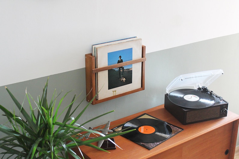 May include: A wooden wall-mounted record rack with vinyl records, a turntable with a clear dust cover, and a record on a wooden table.