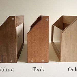 May include: Three wooden magazine holders in different wood finishes: walnut, teak, and oak. Each holder has a slanted front and a clear acrylic panel on the front.