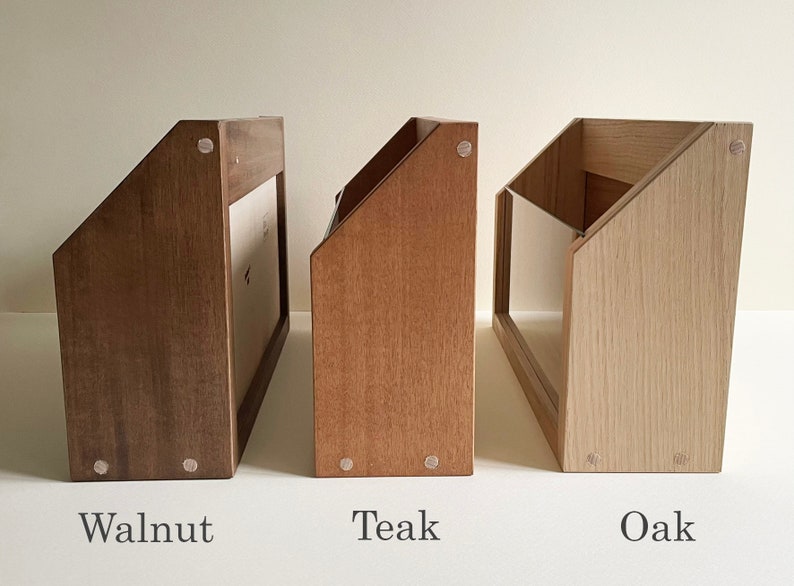 May include: Three wooden magazine holders in different wood finishes: walnut, teak, and oak. Each holder has a slanted front and a clear acrylic panel on the front.