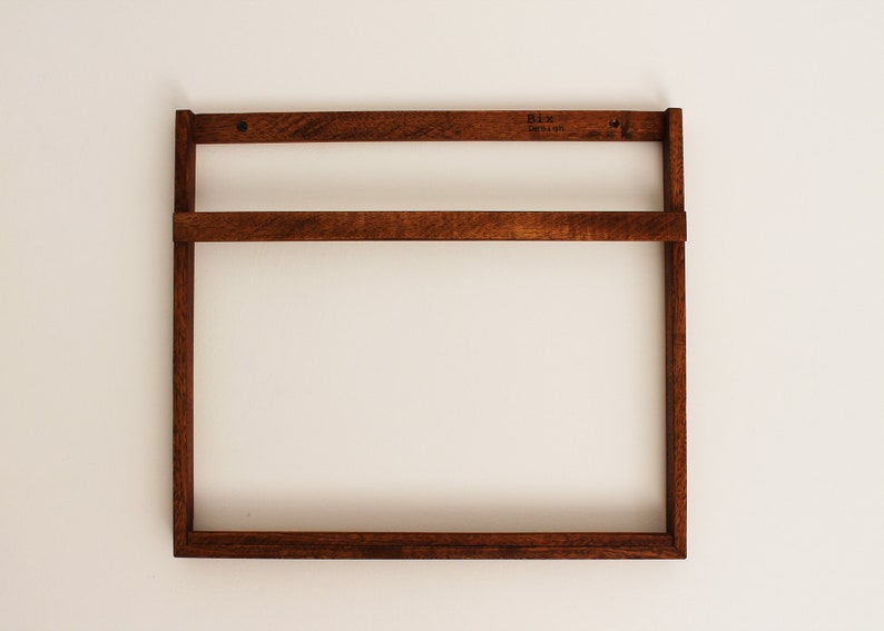 May include: A dark brown wooden wall shelf with two shelves. The shelf is mounted on a white wall. The shelf has a label that says "Bix Design".