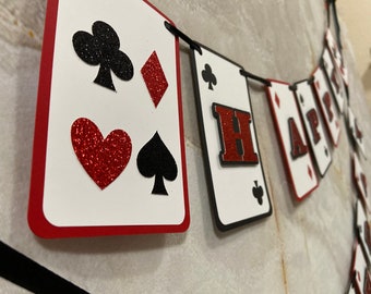 May include: A red, white, and black card-themed banner with the word "HAPPY" spelled out. Each card features a different playing card suit, including hearts, diamonds, spades, and clubs.