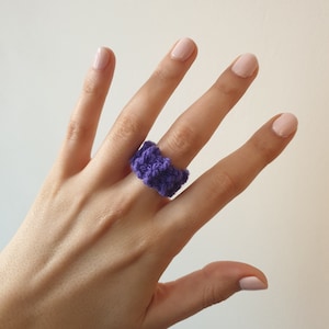 Puede incluir: Un anillo de crochet morado en una mano.