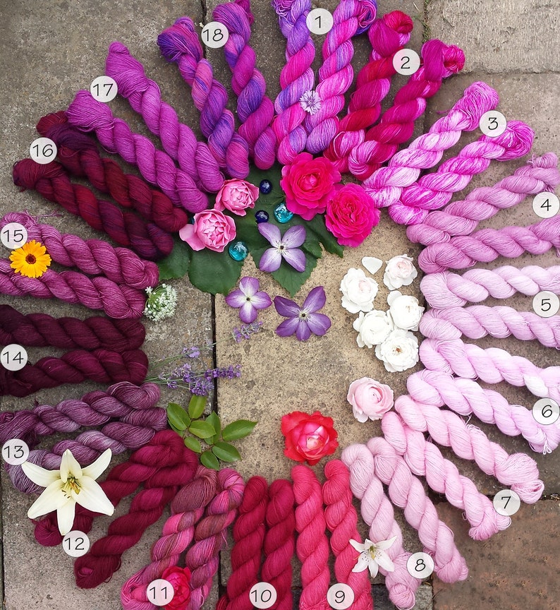 May include: A collection of 18 skeins of yarn in shades of pink, purple, and red arranged in a circle. The yarn is hand-dyed and has a gradient effect. The skeins are numbered 1 through 18.