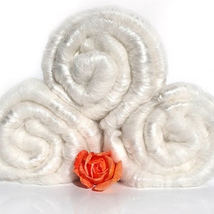 May include: Three rolls of white silk fiber, arranged in a pyramid shape, with a single orange rose in front.