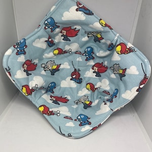 May include: A blue fabric bowl with a white background and a pattern of cartoon superheroes. The superheroes are flying in the air with clouds behind them. The superheroes include Captain America, Iron Man, Thor, Spider-Man, and Black Widow.