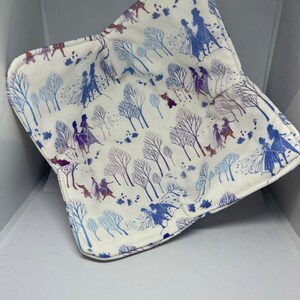 May include: A white fabric burp cloth with a blue and purple pattern of silhouettes of characters from the movie Frozen walking through a snowy forest.