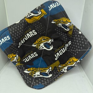 May include: A square bowl cozy featuring a black background with a repeating pattern of Jacksonville Jaguars logos in teal, gold, and white. The words "Jaguars" and "Jacksonville Jaguars" are visible.
