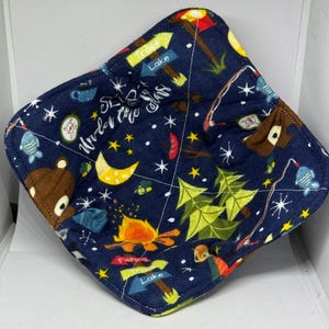 May include: A blue fabric pot holder with a camping theme. It features a campfire, stars, trees, and the text "Sleep Under the Stars".
