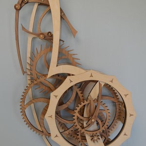 May include: Wooden wall clock with intricate gear and cog design. The clock features a light wood finish with darker wood accents, creating a layered, three-dimensional effect. The clock's design includes multiple gears and a pendulum, showcasing a unique, artistic style.