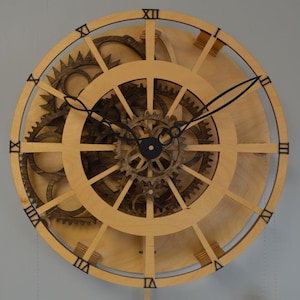 Pu&ograve; includere: Un orologio in legno con numeri romani e ingranaggi intricati visibili dietro il quadrante. L'orologio ha lancette nere e un pendolo.
