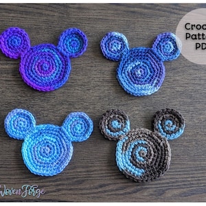 May include: Four crocheted mouse-shaped coasters in blue and brown color combinations. The coasters are made with a spiral pattern and are arranged on a wooden surface. The text "Crochet Pattern PDF" is visible in the top right corner of the image.
