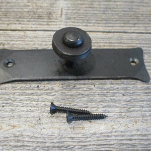 May include: A dark gray metal cabinet door pull with a round knob and a rectangular backplate. Two black screws are included. The hardware is designed for a rustic or industrial aesthetic.
