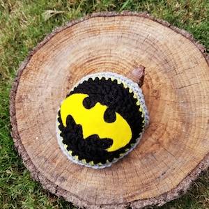 Könnte beinhalten: Eine graue Häkelmütze mit einem gelben Filz-Batman-Logo.