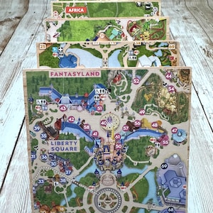 May include: A colorful map of a theme park, divided into sections with different names, including "Fantasyland" and "Liberty Square". Each section is numbered with a corresponding number on the map. The map is made of wood and has a worn, vintage look.