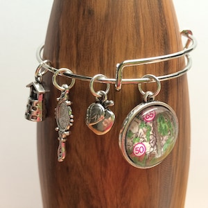 May include: A silver charm bracelet with multiple charms, including a house, a mirror, a heart, and a round charm with a map and numbers 50 and 65.
