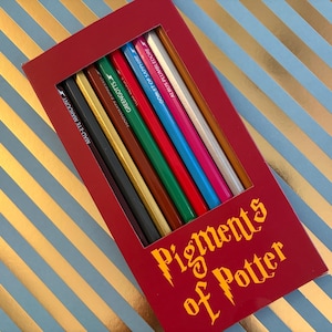 May include: A red box of colored pencils with the text "Pigments of Potter" in gold lettering. The pencils are various colors, including black, gold, green, red, pink, and blue. The pencils are labeled with names like "Mad-Eye Moody" and "Gringotts".