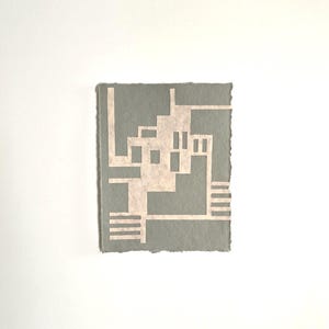 Puede incluir: Una peque&ntilde;a obra de arte rectangular con un dise&ntilde;o geom&eacute;trico. La obra de arte tiene un fondo gris claro con un patr&oacute;n geom&eacute;trico m&aacute;s claro, blanquecino. Los bordes de la obra de arte son &aacute;speros y desiguales, d&aacute;ndole una apariencia hecha a mano.