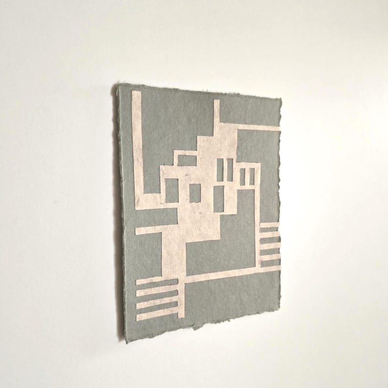 Puede incluir: Una obra de arte rectangular gris con un dise&ntilde;o geom&eacute;trico en rosa claro. La obra de arte tiene una superficie rugosa y texturizada y un borde rasgado. El dise&ntilde;o presenta l&iacute;neas rectas y formas rectangulares.