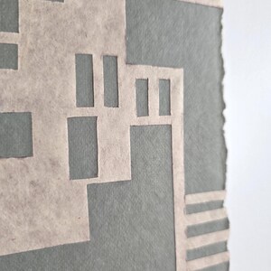 Puede incluir: Obra de arte abstracta con un dise&ntilde;o geom&eacute;trico en beige claro sobre un fondo gris. La obra tiene una apariencia texturizada y un borde rasgado. El dise&ntilde;o incorpora formas rectangulares y lineales.