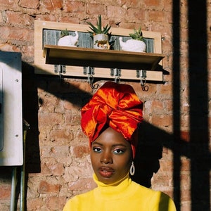 white acrylic statement earrings on model with red hair wrap and yellow turtleneck against brick wall