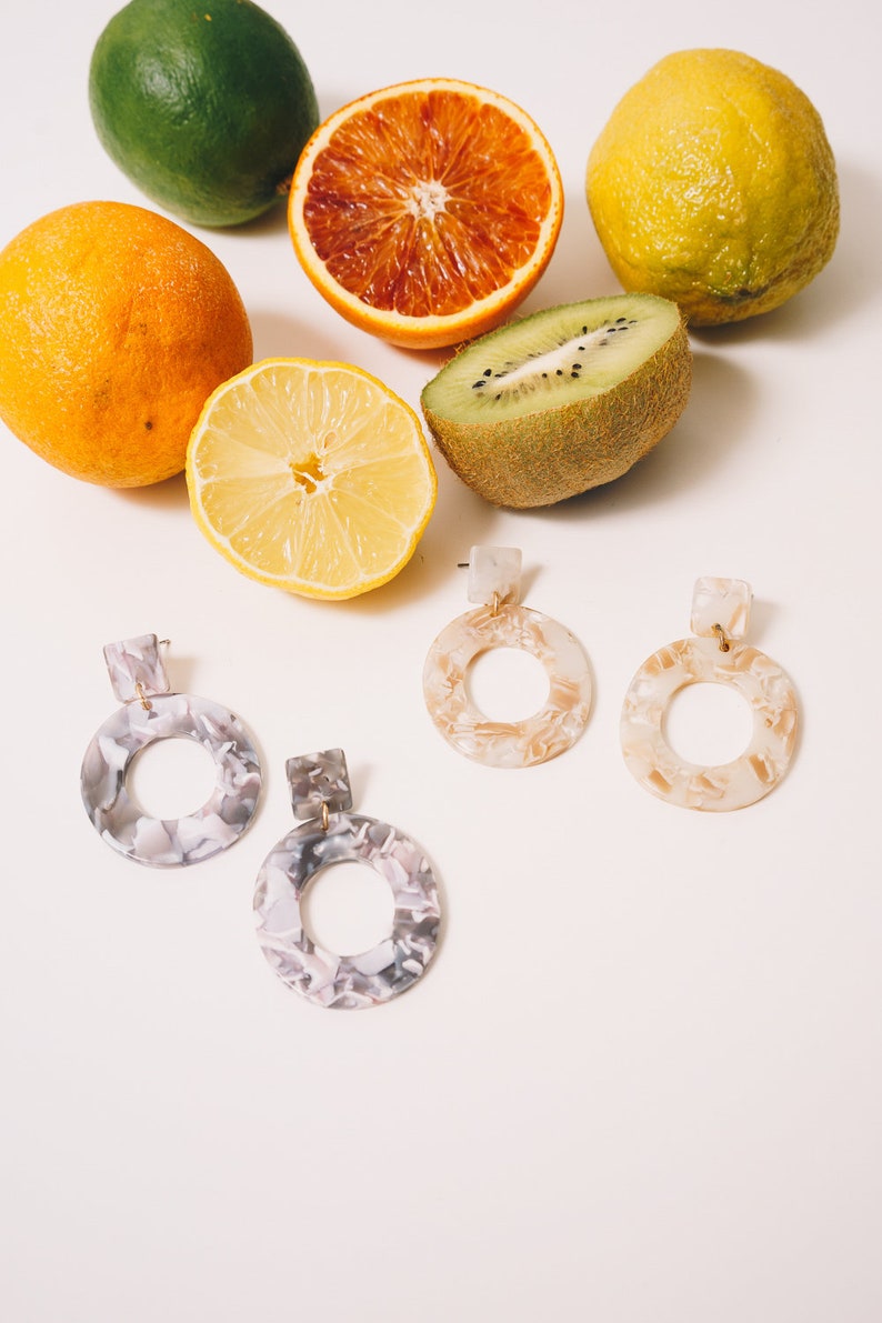 grey multicolored oval acrylic earrings with tan multicolored acrylic earrings with cut citrus in the background