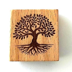 May include: A square wooden stamp featuring a dark brown laser-engraved design of a tree with a full canopy of leaves and visible roots extending downwards. The natural light-coloured wood grain is clearly visible across the entire surface.
