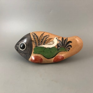 May include: Hand-painted ceramic fish figurine with a white bird, green foliage, and orange accents. The fish has a black eye and a brown and black body.