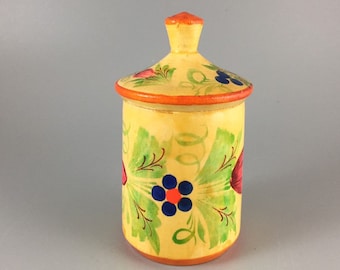 May include: A small, yellow wooden jar with a lid, painted with green leaves and red, blue, and orange flowers. The jar is a traditional folk art design.