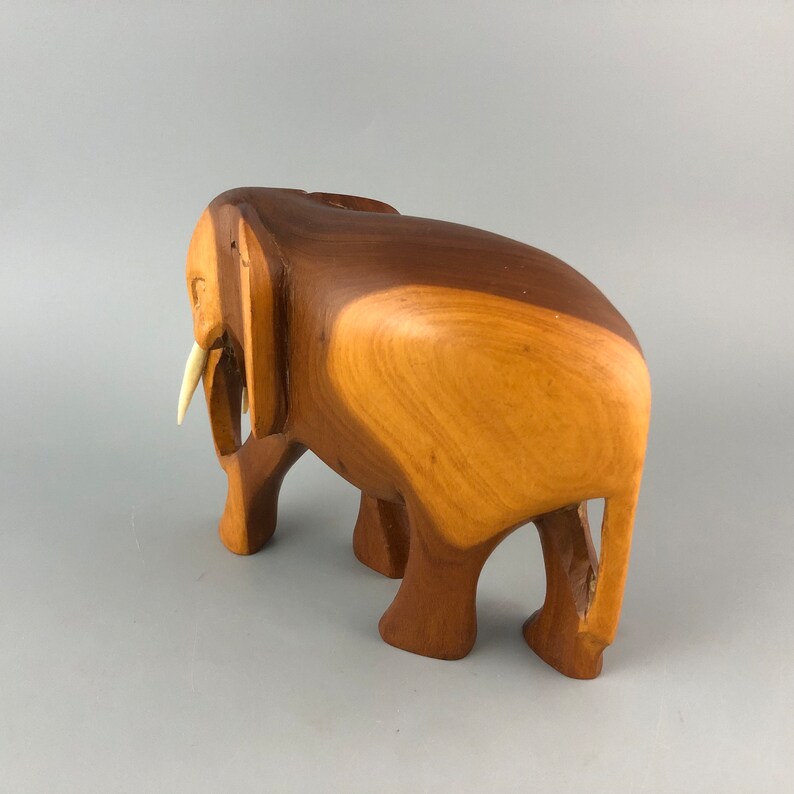 May include: A wooden elephant sculpture with a carved ivory tusk. The elephant is standing with its legs spread apart and its trunk raised. The sculpture is made of a light brown wood with a smooth finish.