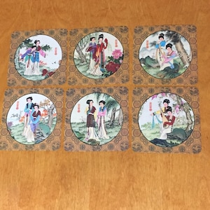 May include: Six square coasters with a gold border and a circular design featuring women in traditional Chinese clothing. The women are depicted in various scenes, including playing music, holding fans, and standing in gardens.