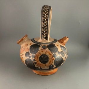 May include: A brown ceramic pitcher with a black and white floral design. The pitcher has a handle and a spout. The pitcher is decorated with flowers and leaves.